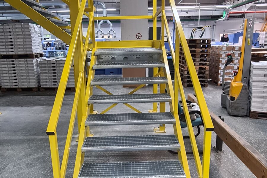 Hallenbüro auf gelber Stahlbühne mit Treppe sorgt für erhöhten Stauraum. Verbaut durch Jansen Systembau