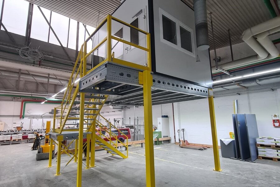 Hallenbüro auf gelber Stahlbühne mit Treppe sorgt für erhöhten Stauraum. Verbaut durch Jansen Systembau